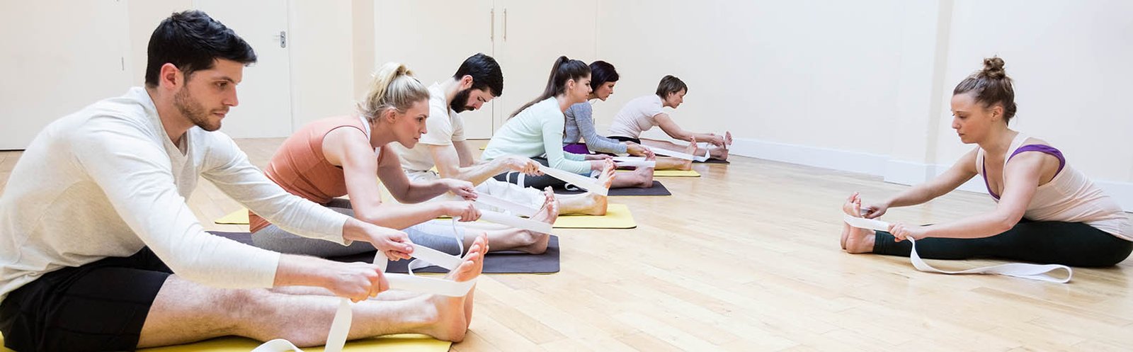 Trainer assisting group of people with stretching exercise in the fitness studio